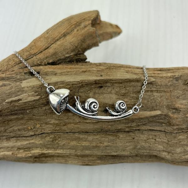mushroom and snail necklace displayed on a piece of wood