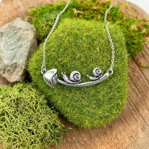 snail and mushroom necklace displayed on a moss